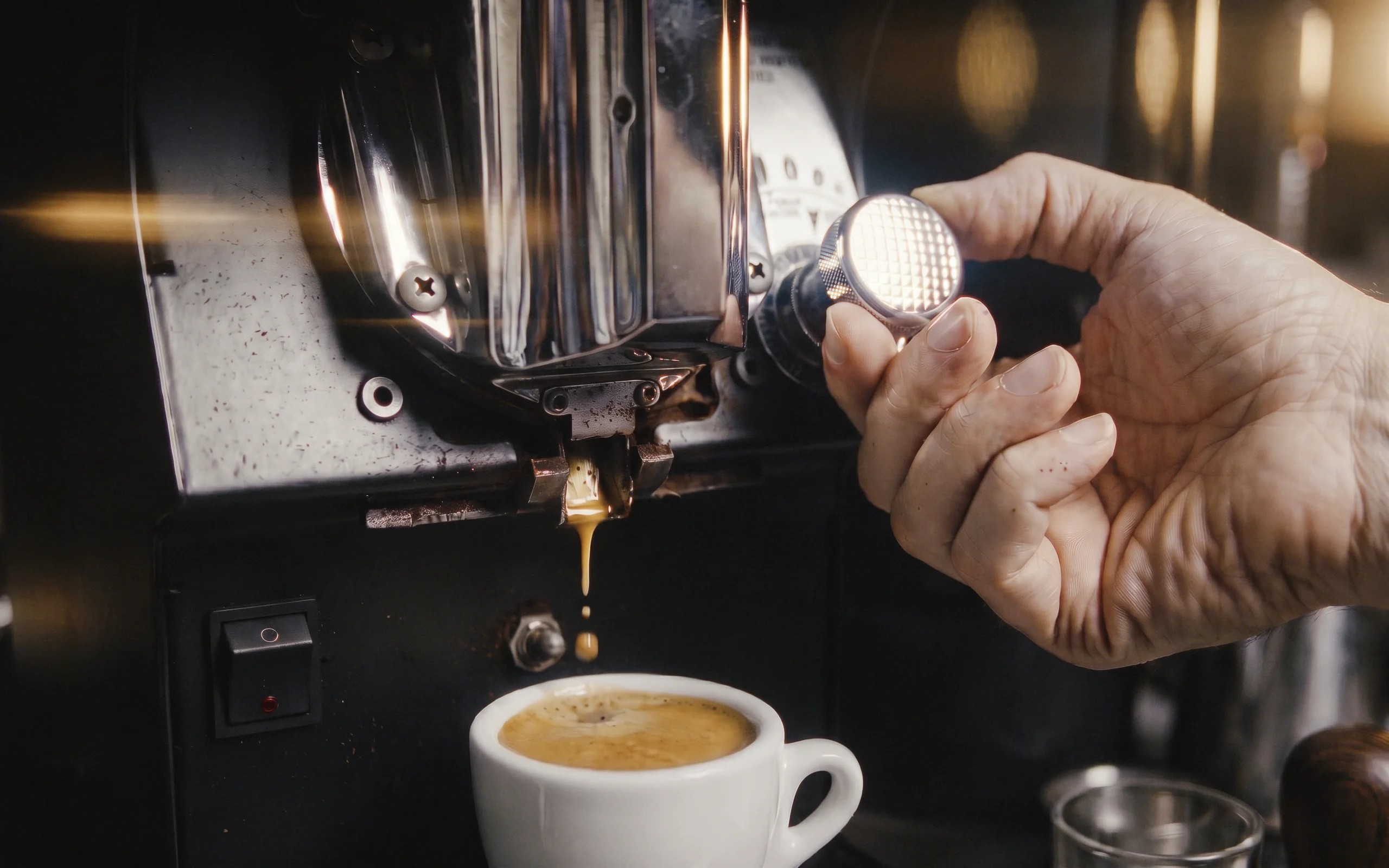 Mano ajustando el dial de molienda de un molino Mythos mientras dispensa café sobre una taza de espresso.