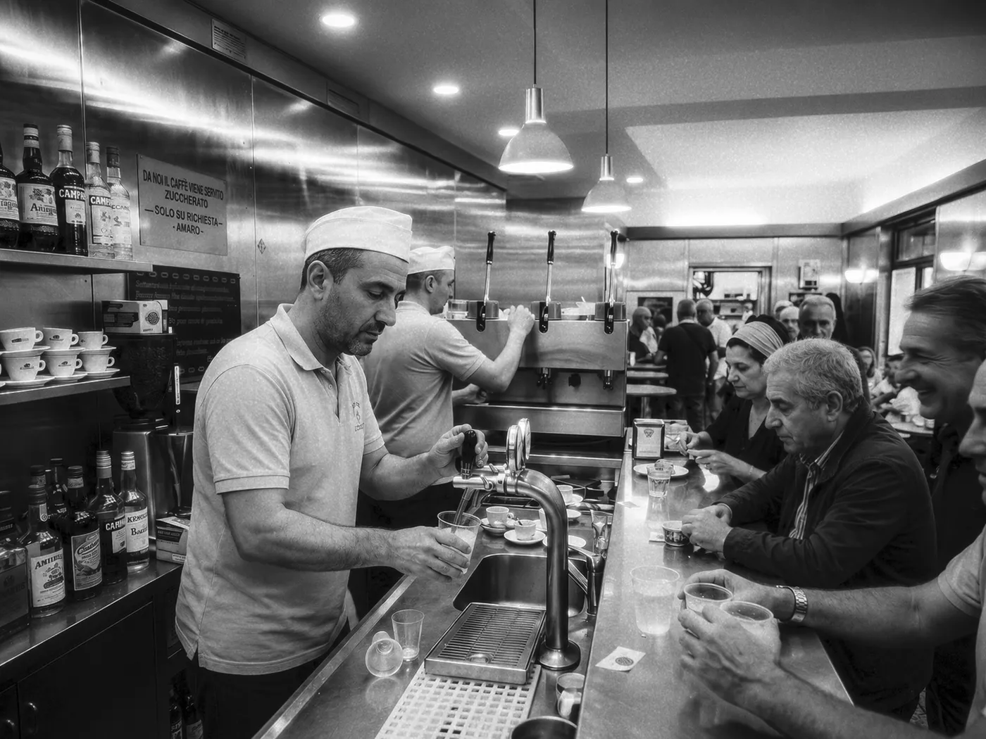 Barra de café napolitana con clientes de pie y camareros trabajando detrás del mostrador.