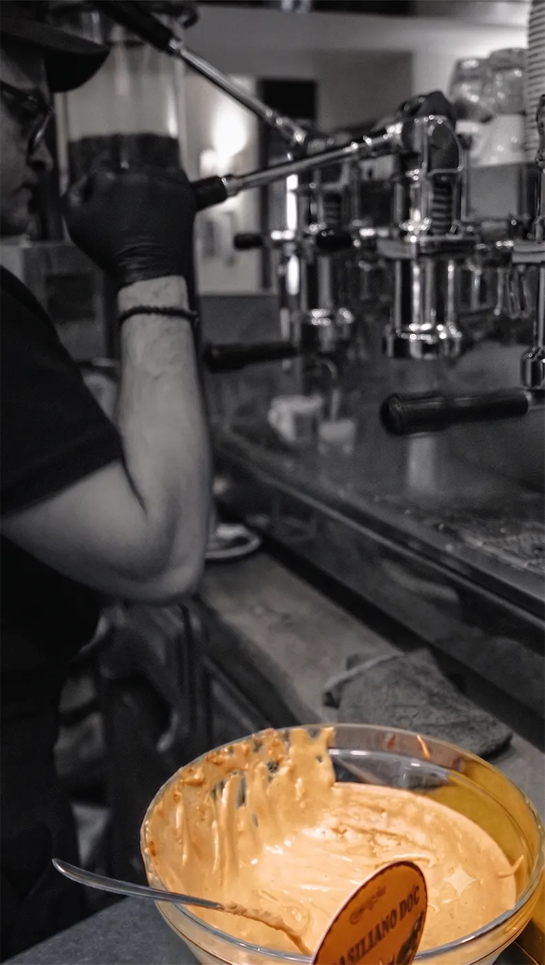 Barista junto a una máquina de espresso con un cuenco de cremina preparado al lado.